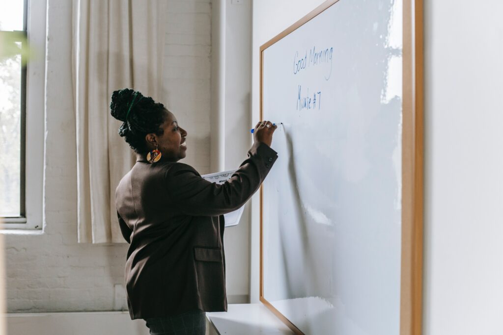 Cheerful teacher writing on whiteboard in classroom